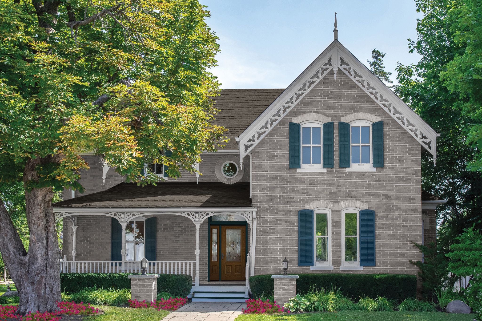 This brick home has white gingerbread trim, blue shutters, a wooden door and a front porch.