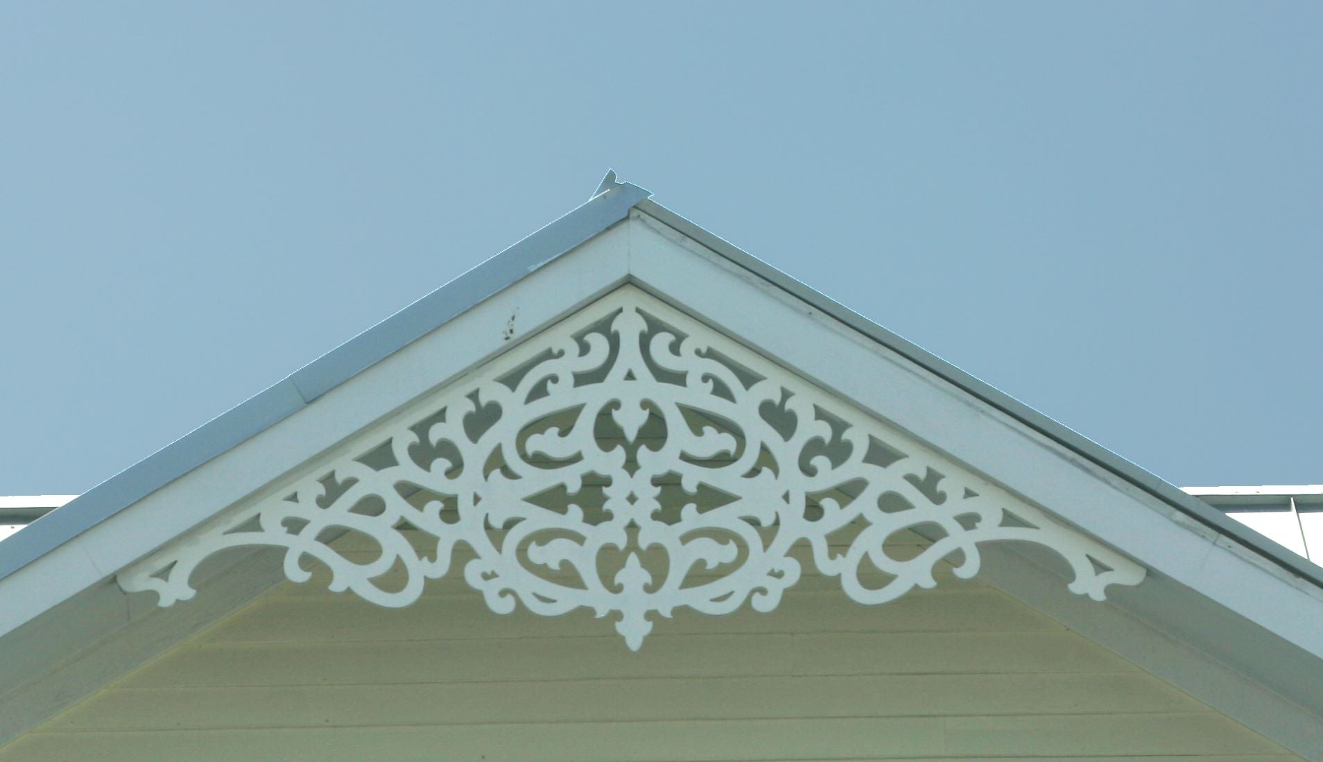 This is a close-up image of white gingerbread gable trim on a yellow home.