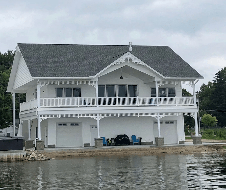 This lakefront home has a white PVC wrap around porch railing and Victorian-style gable decoration.