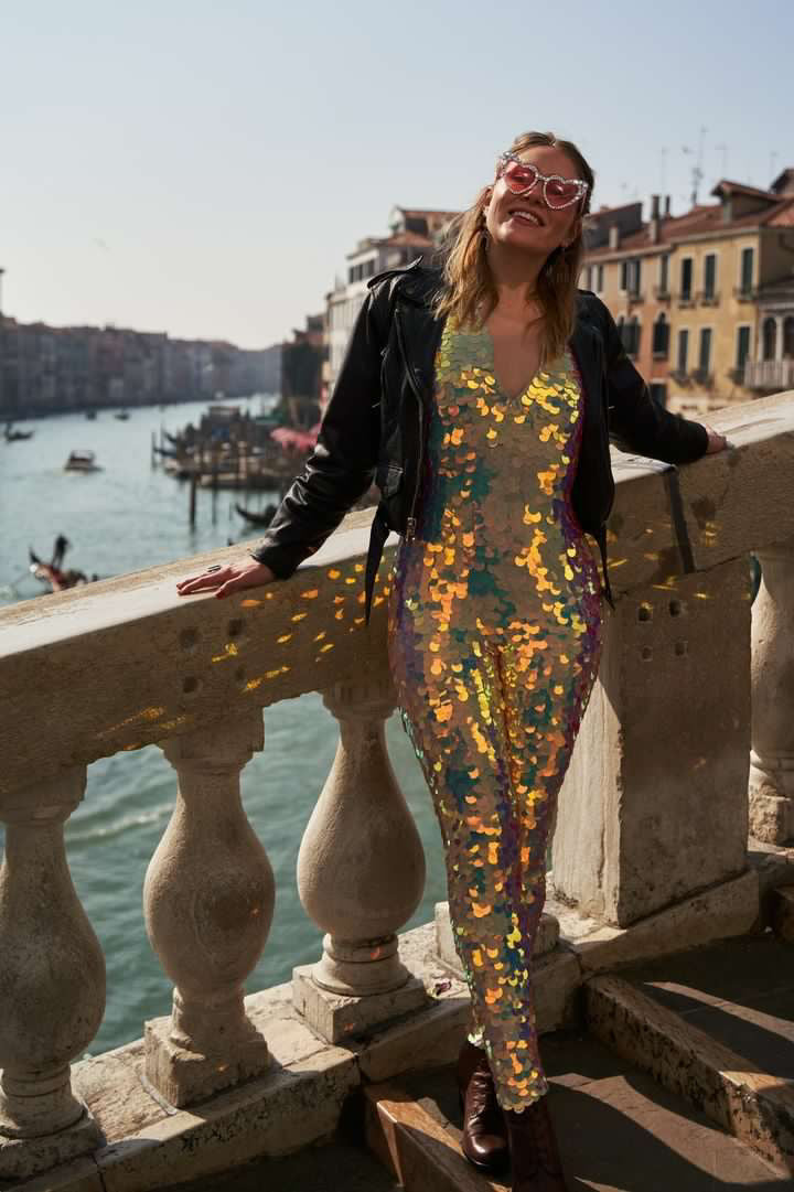 Woman smiling on a sunny day in heart sunglasses and Rosa Bloom Sequin Jumpsuit in a soft Rose colour on St Marks Bridge in Venice