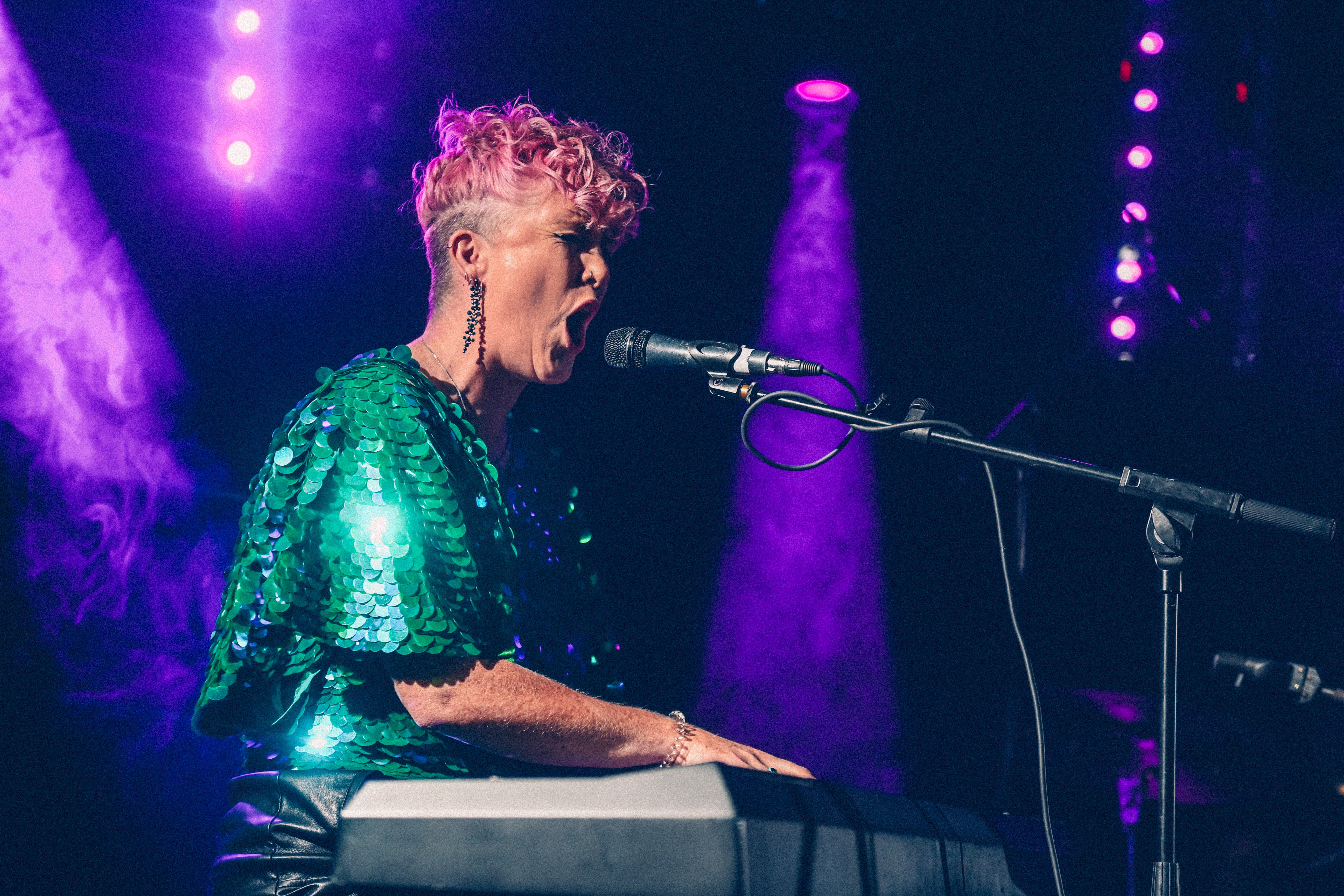 Woman in all sequin jumpsuit by Rosa Bloom singing on stage at a festival