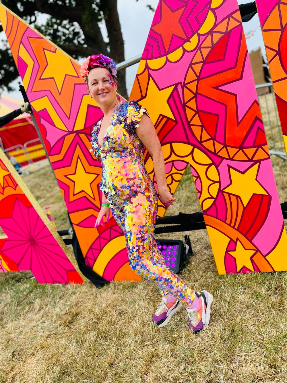 Smiling woman wearing pink and purple sequin Rosa Bloom Aphrodite Jumpsuit posing in front of a colourful letter at a festival