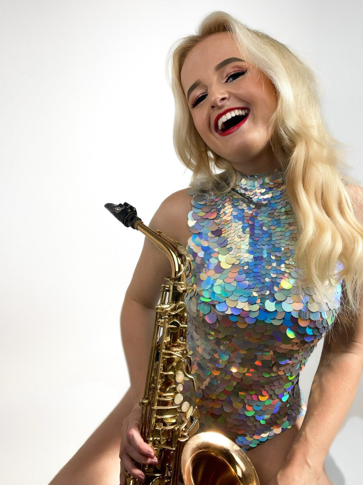 Blonde saxophonist smiling in red lipstick holding a saxophone wearing a hologram silver Fifi sequin Rosa Bloom leotard