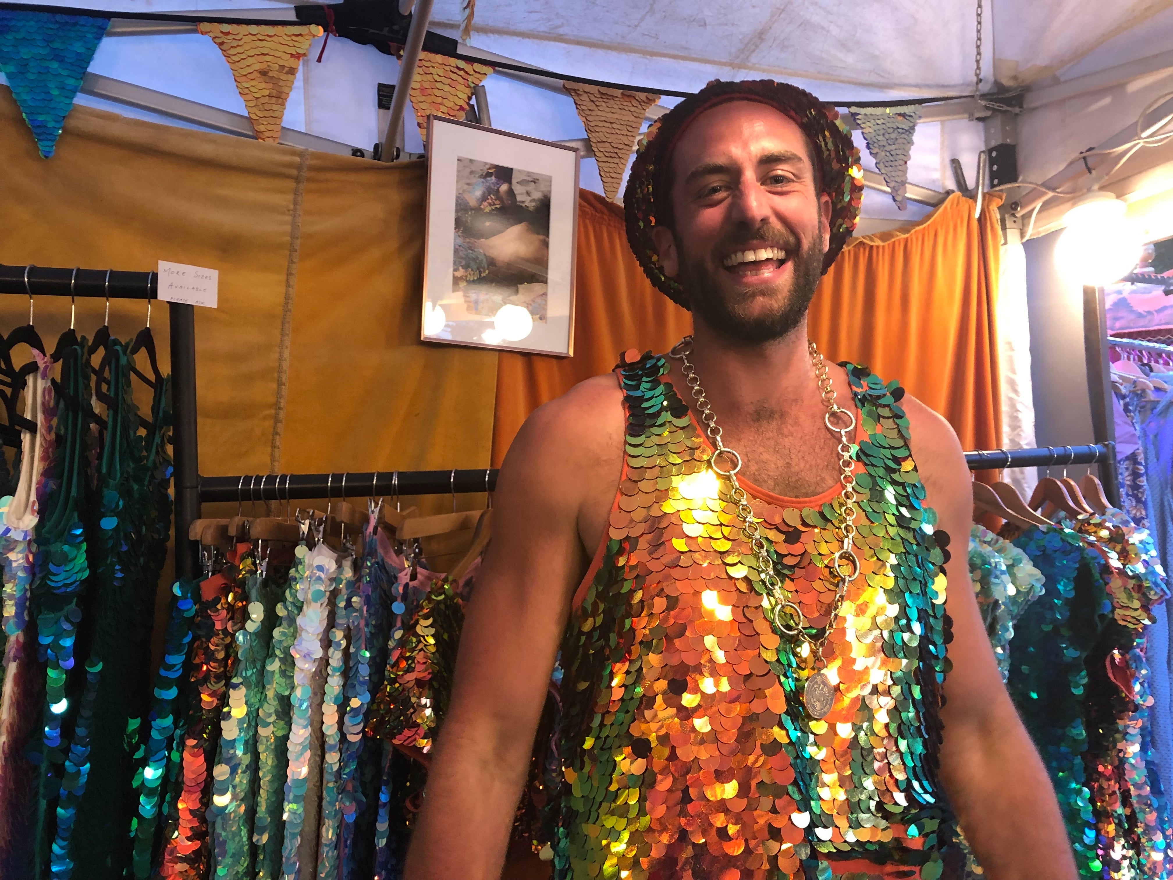 Tall man laughing joyfully inside the Rosa Bloom stall at Wilderness Festival wearing a Rosa Bloom Ember sequin beret, and sequin vest top