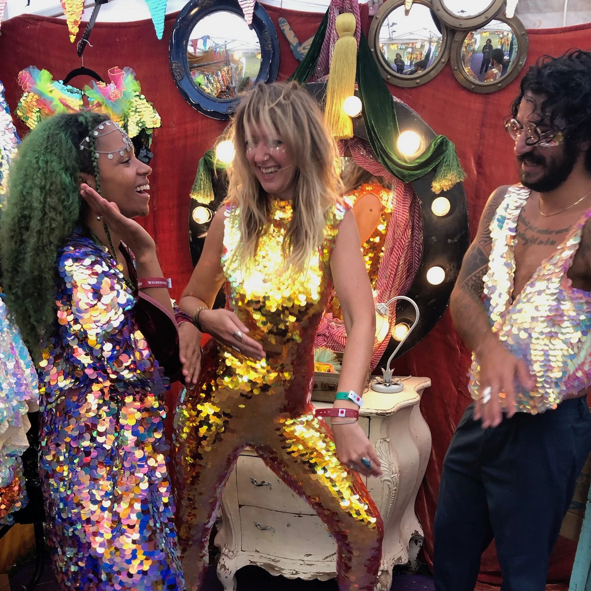 Three members of staff at the Rosa Bloom fesitival pop up shop dance together while wearing bright sequin outfits.