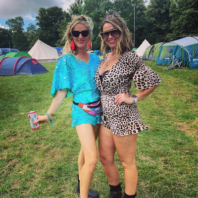 Two festival goes pose for a photo in the camping field and one wears an eye-catching bright blue sequin romper. 