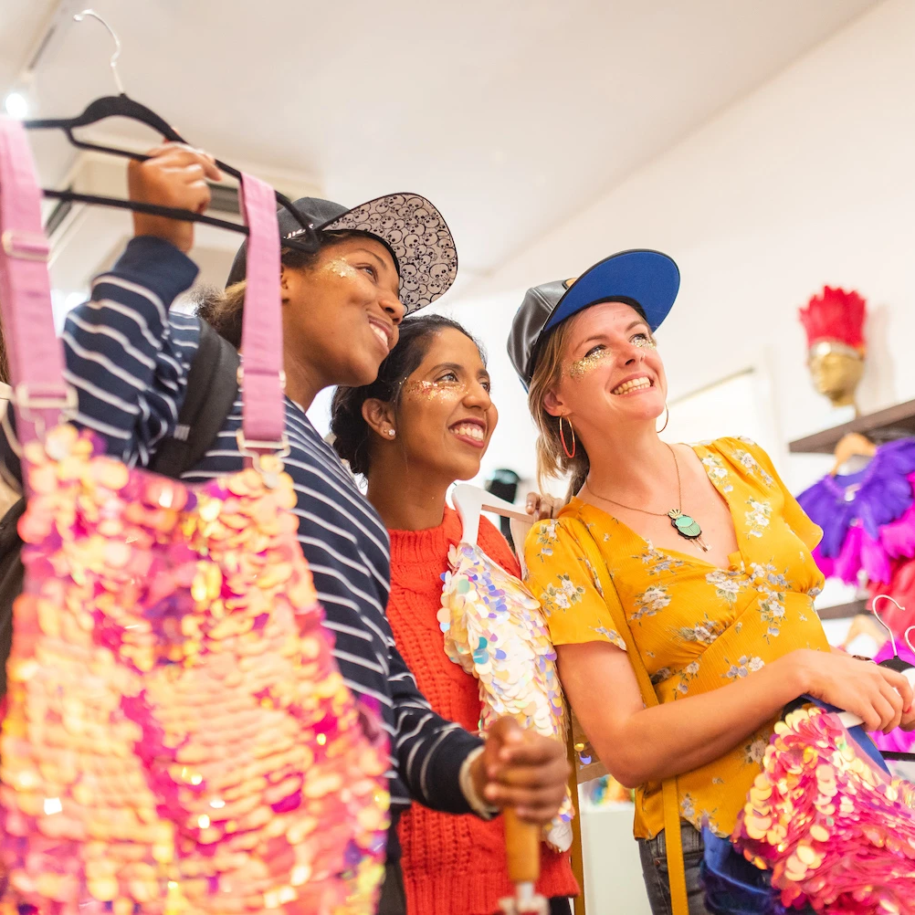 Three female friends at the slow fashion brand Rosa Bloom pop up shop stand together while holding pink sequin clothing.