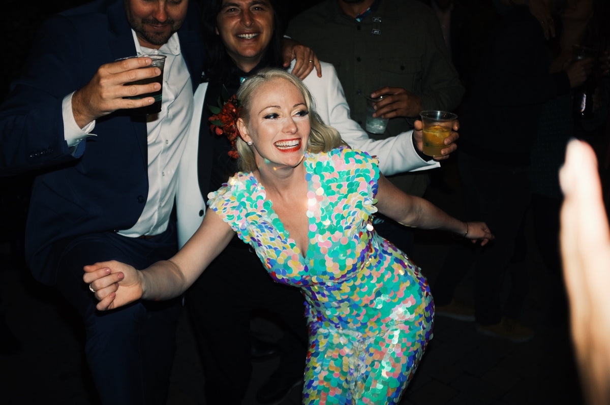 A festivsl bride dances at her wedding and wears a white sequin jumpsuit