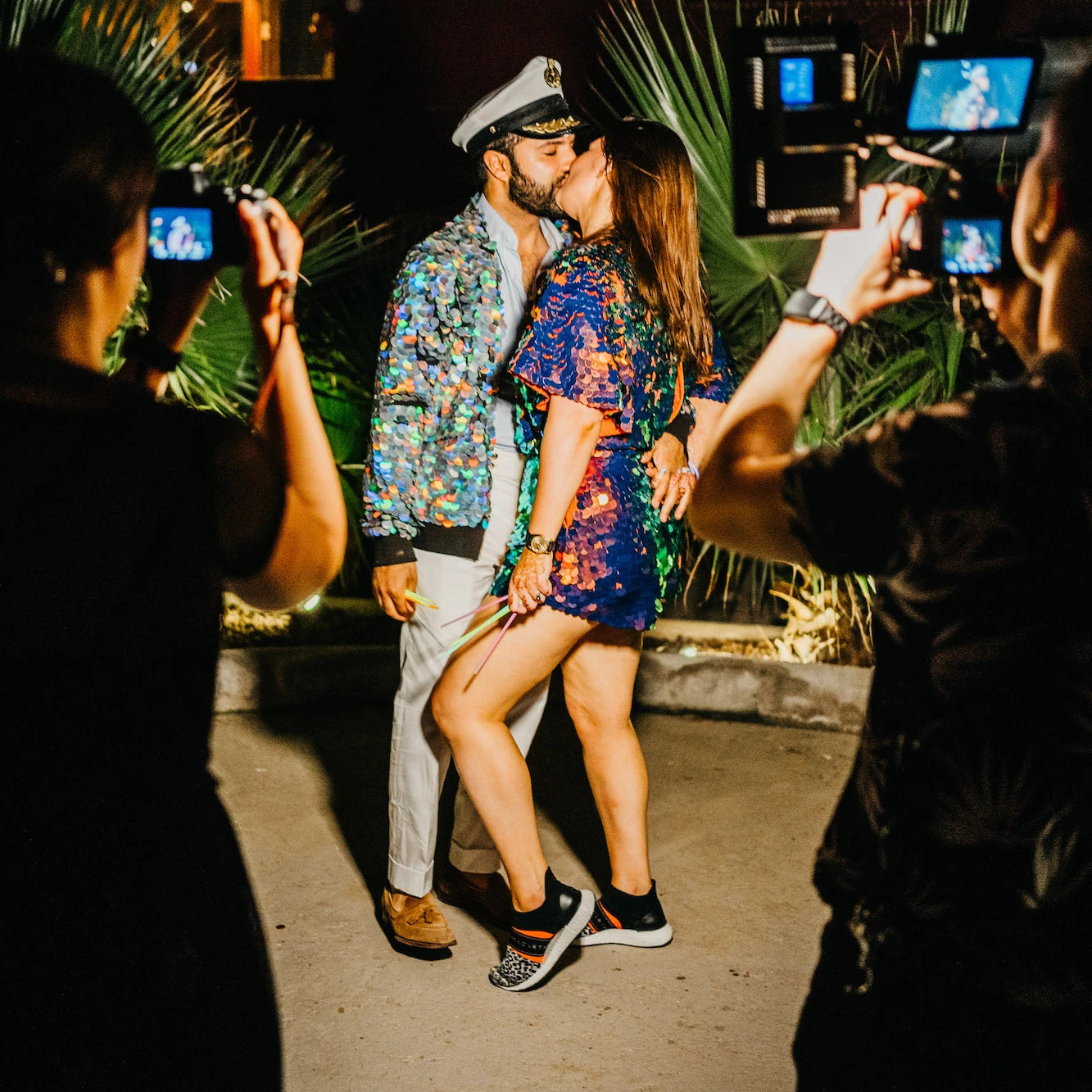 A bride and groom in sequin outfits share a kiss