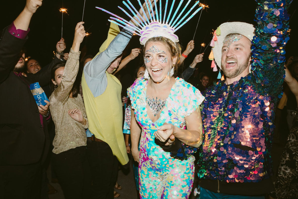 A bride and groom wearing festival inspired sequin outfits take to the dancefloor