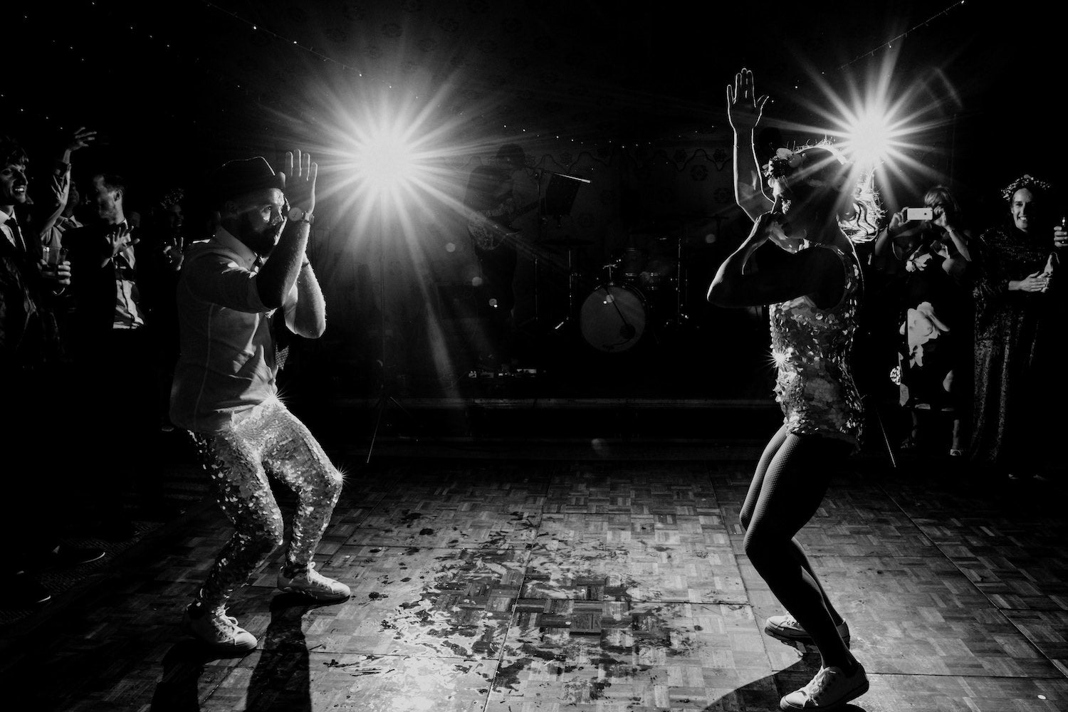 A black and white image of a bride a groom wearing matching sequin outfits poerforming their first dance at their wedding reception.