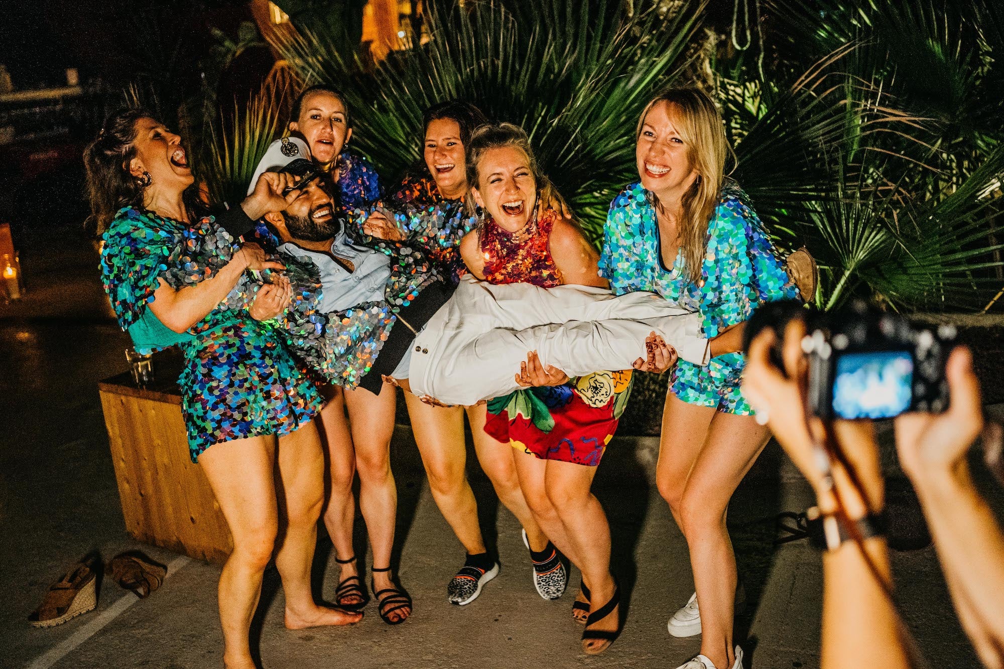 A bridal party wearing sequins carry the groom 