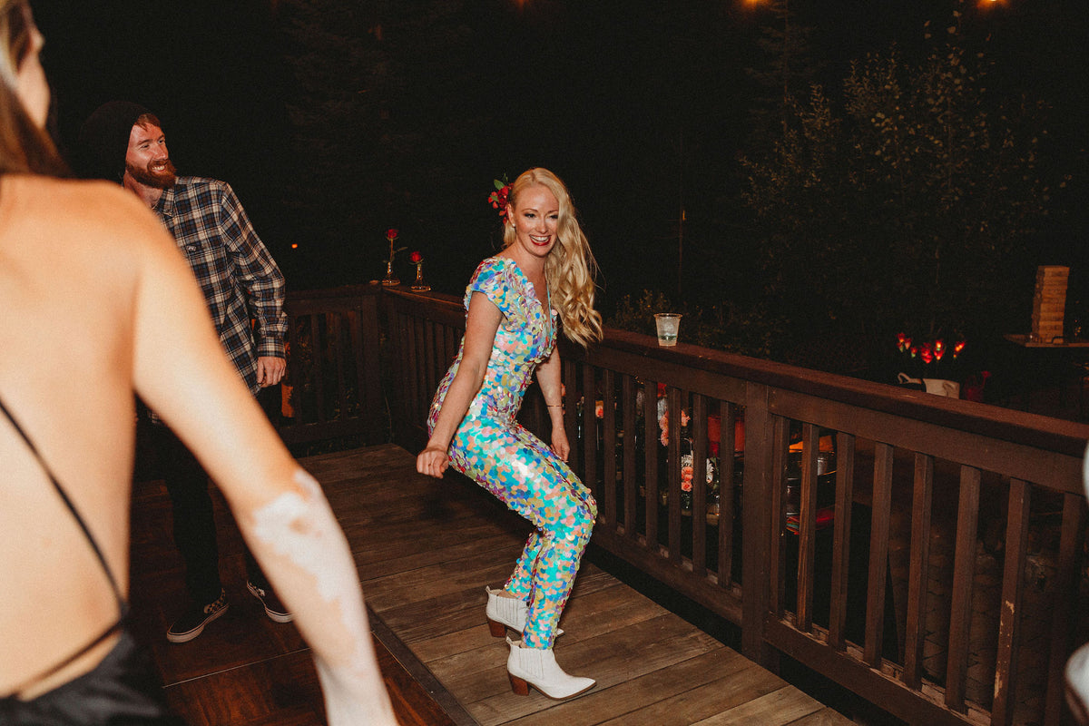 A bride wearing festival style white sequin jumpsuit with white cowboy boots dances at her wedding. 