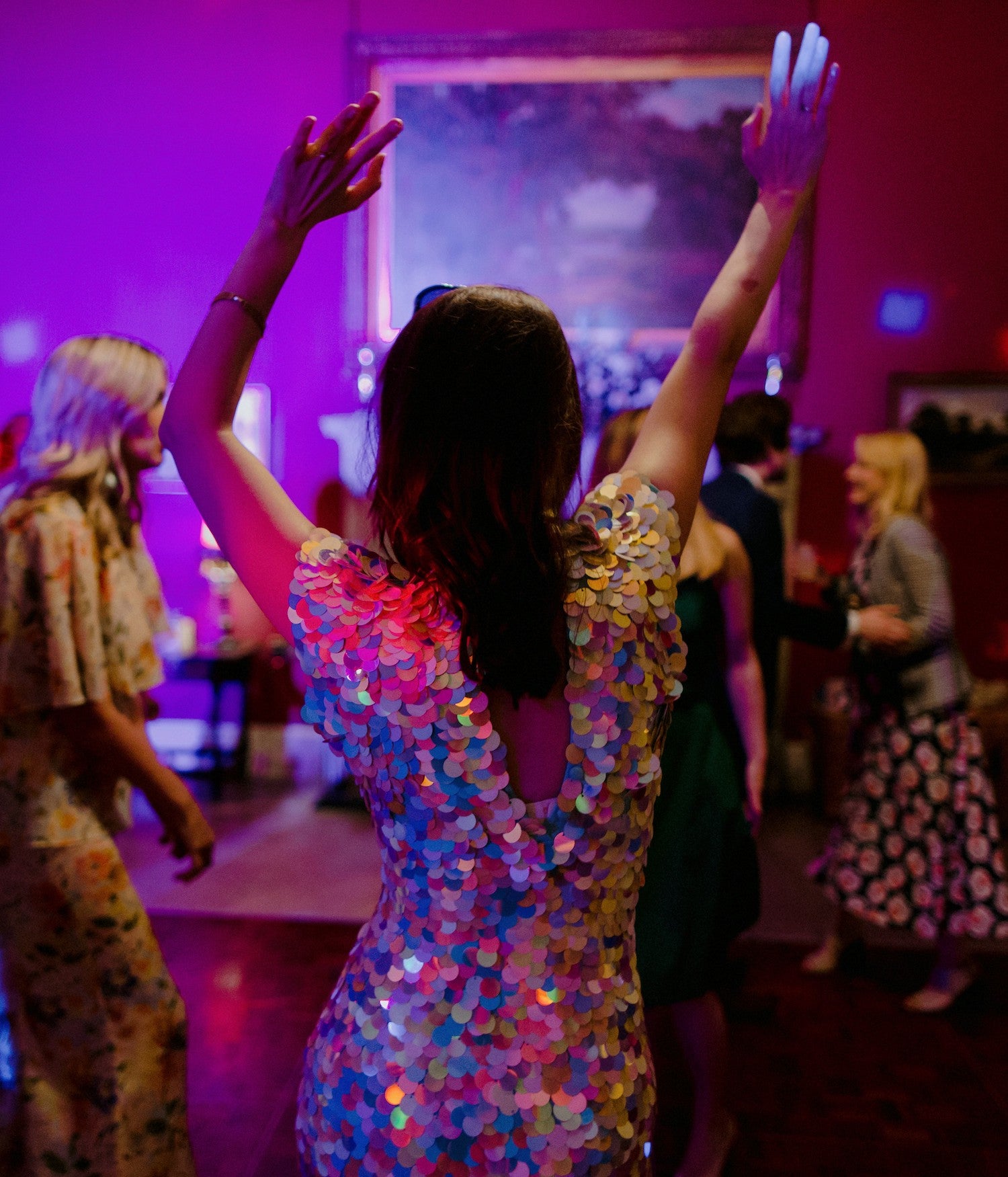 A bride wearing a sequin jumpsuit covered in large white iridescent sequins dances at her wedding reception. 