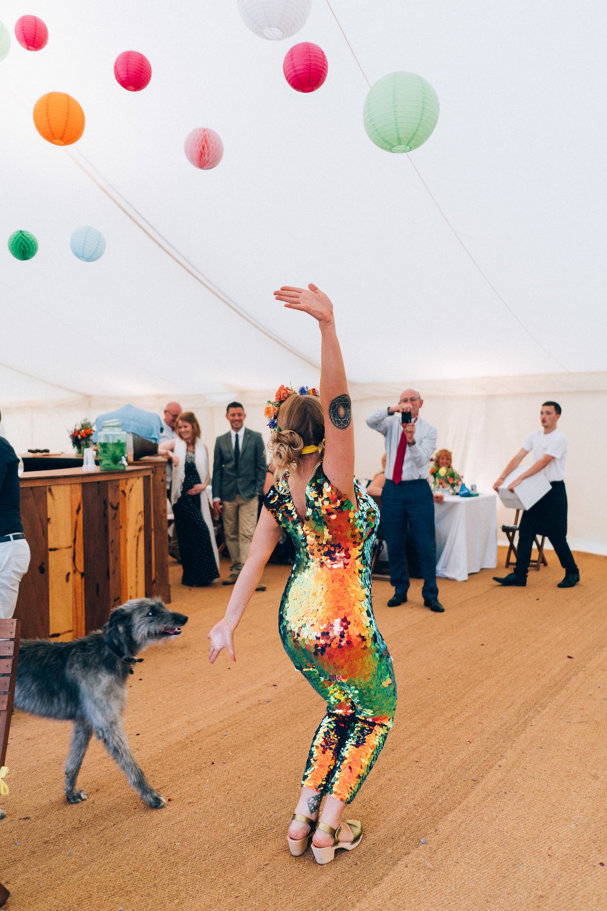 A bride wearing a festival style red sequin jumpsuit strikes a pose on the dancefloor at her wedding. 