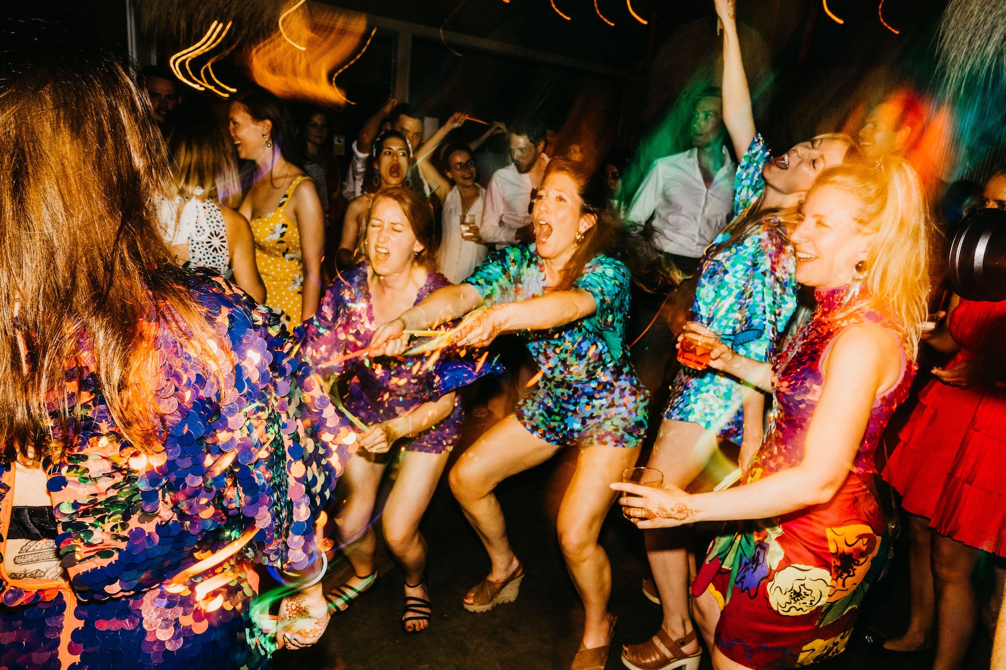 Bridesmaids in sequin playsuits dance at a wedding