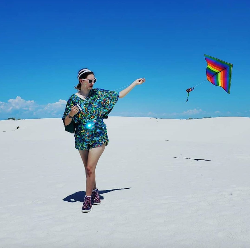 A woman in a sequin romper flying a rainbow kite at White Sands