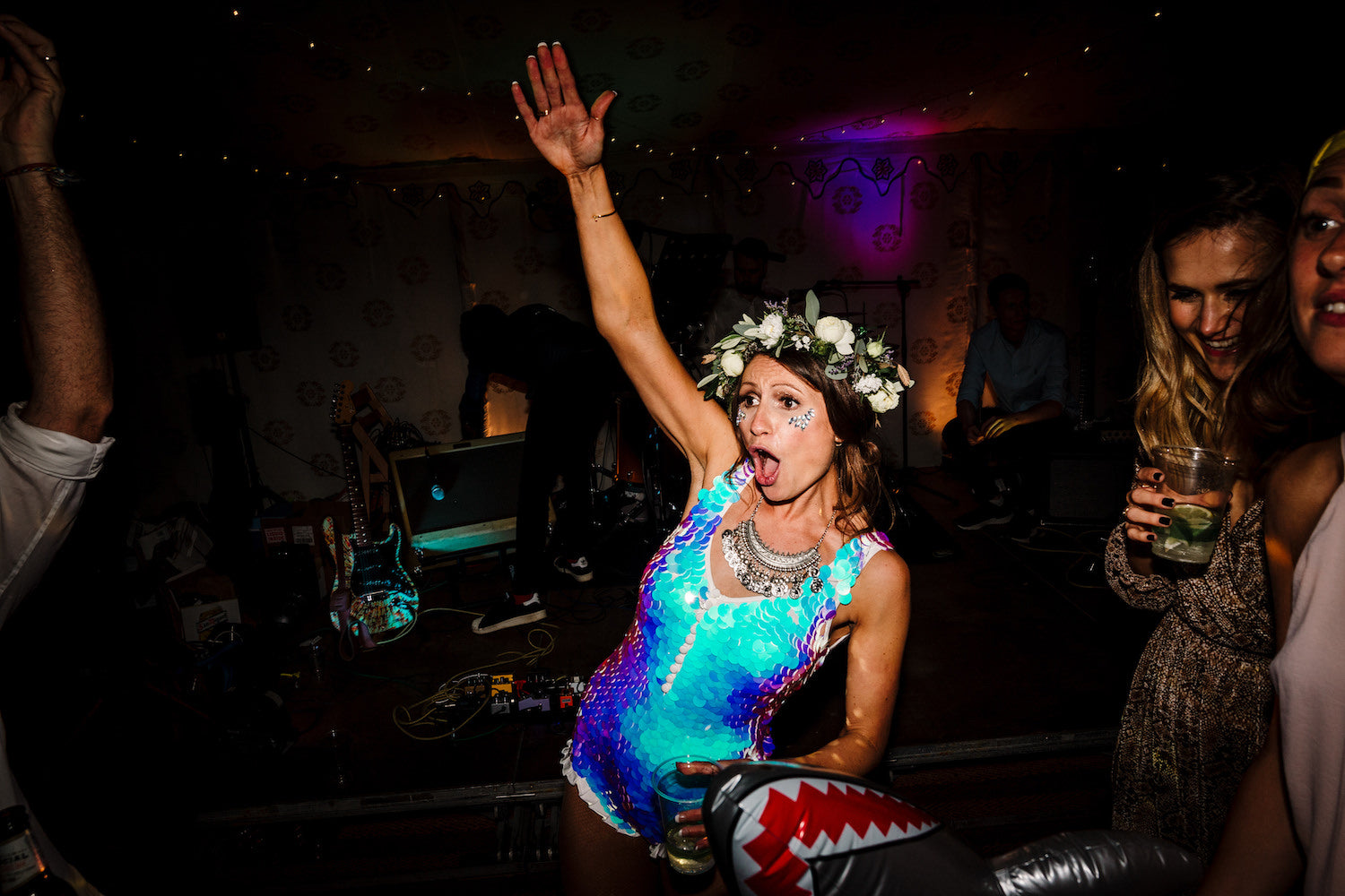 A bride wearing a white sequin playsuit and floral headband dancing at her wedding reception