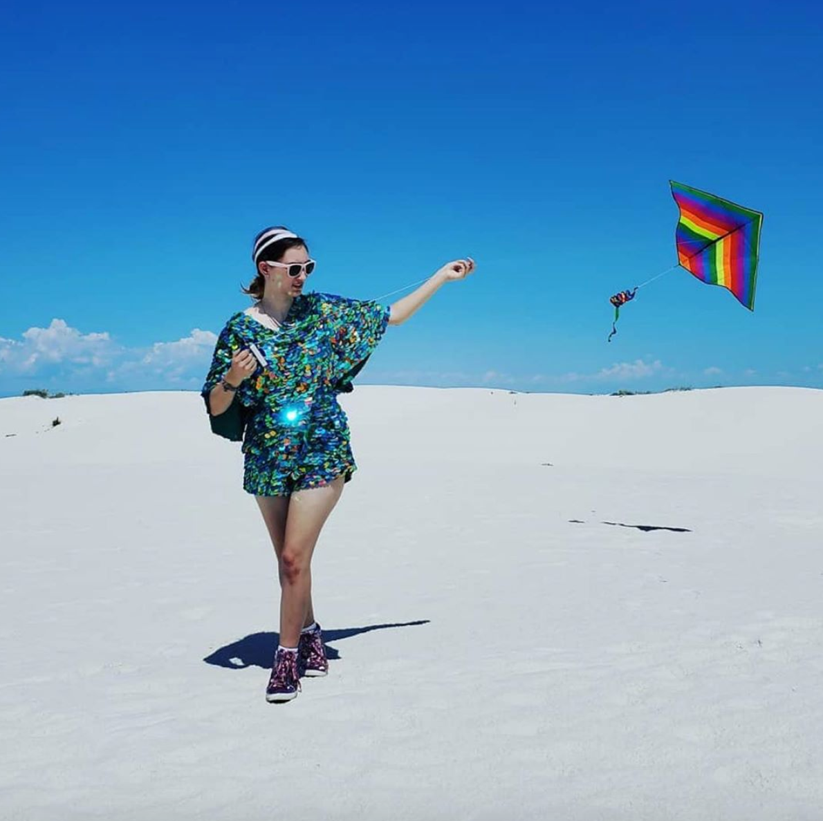 A woman wearing a green sequin romper flies a kite at White Sands