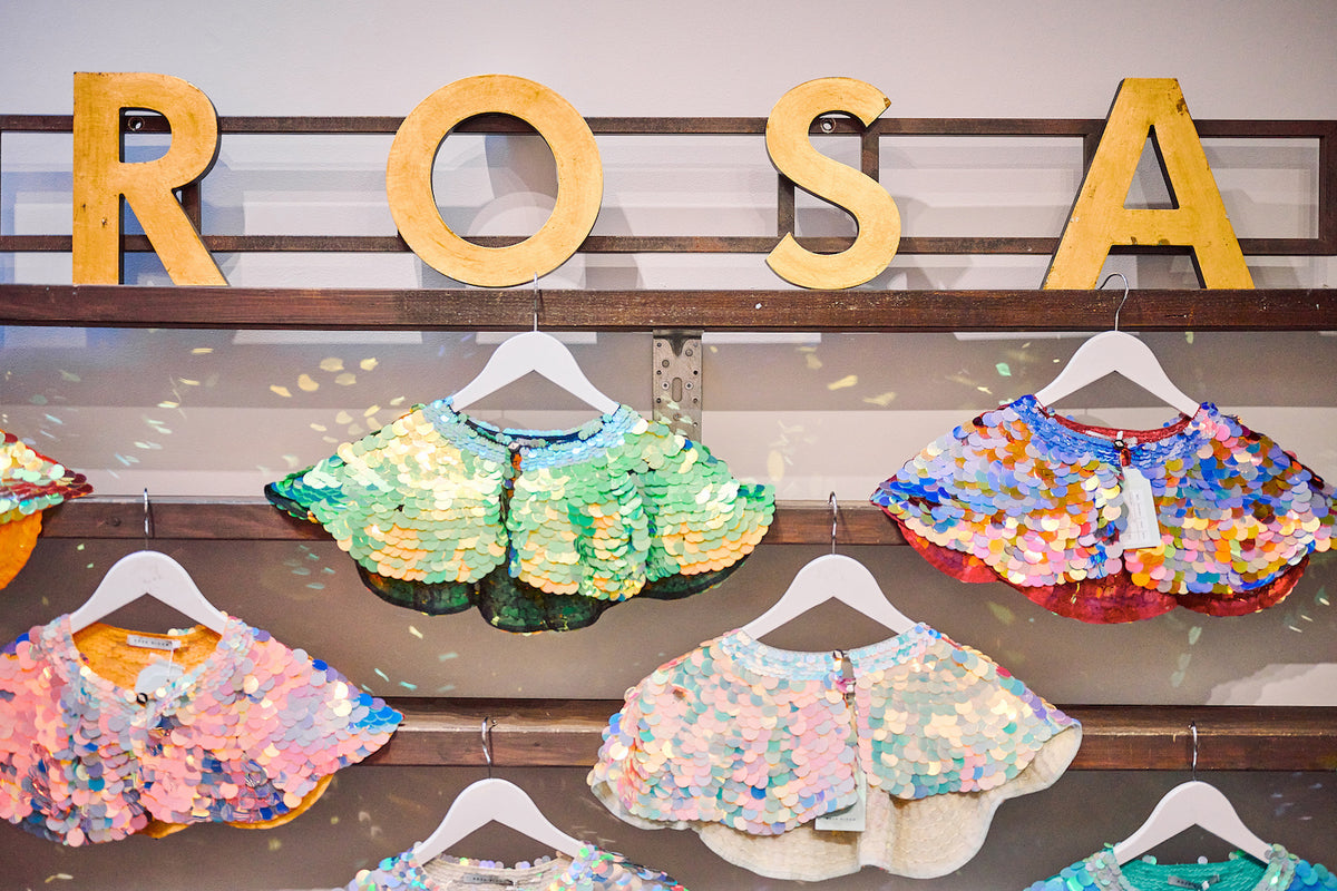 A sign of the word Rosa above a display of sequin capes in various colours.