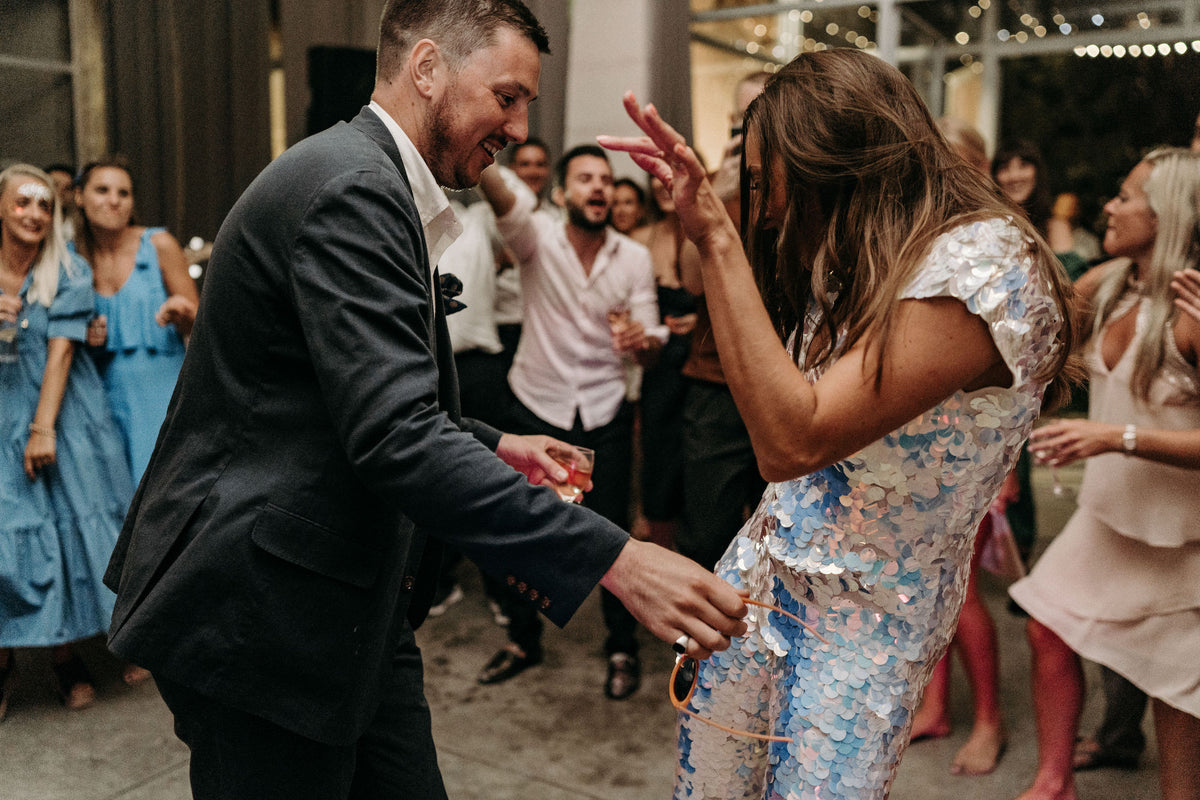 A bride wearing a white sequin jumpsuit dances with the groom