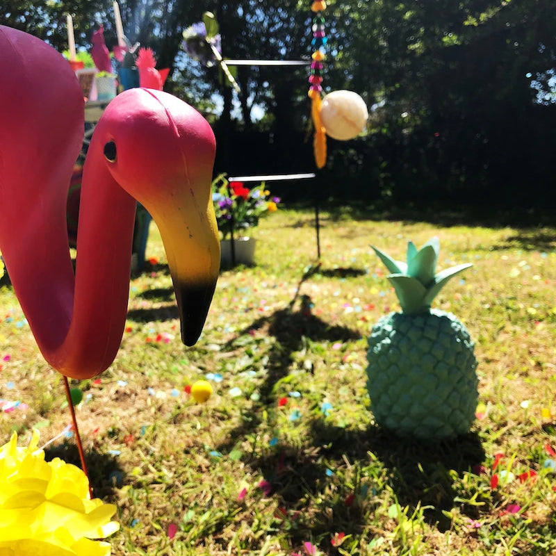 Close up of a plastic flamingo in a garden stood by a plastic pineapple