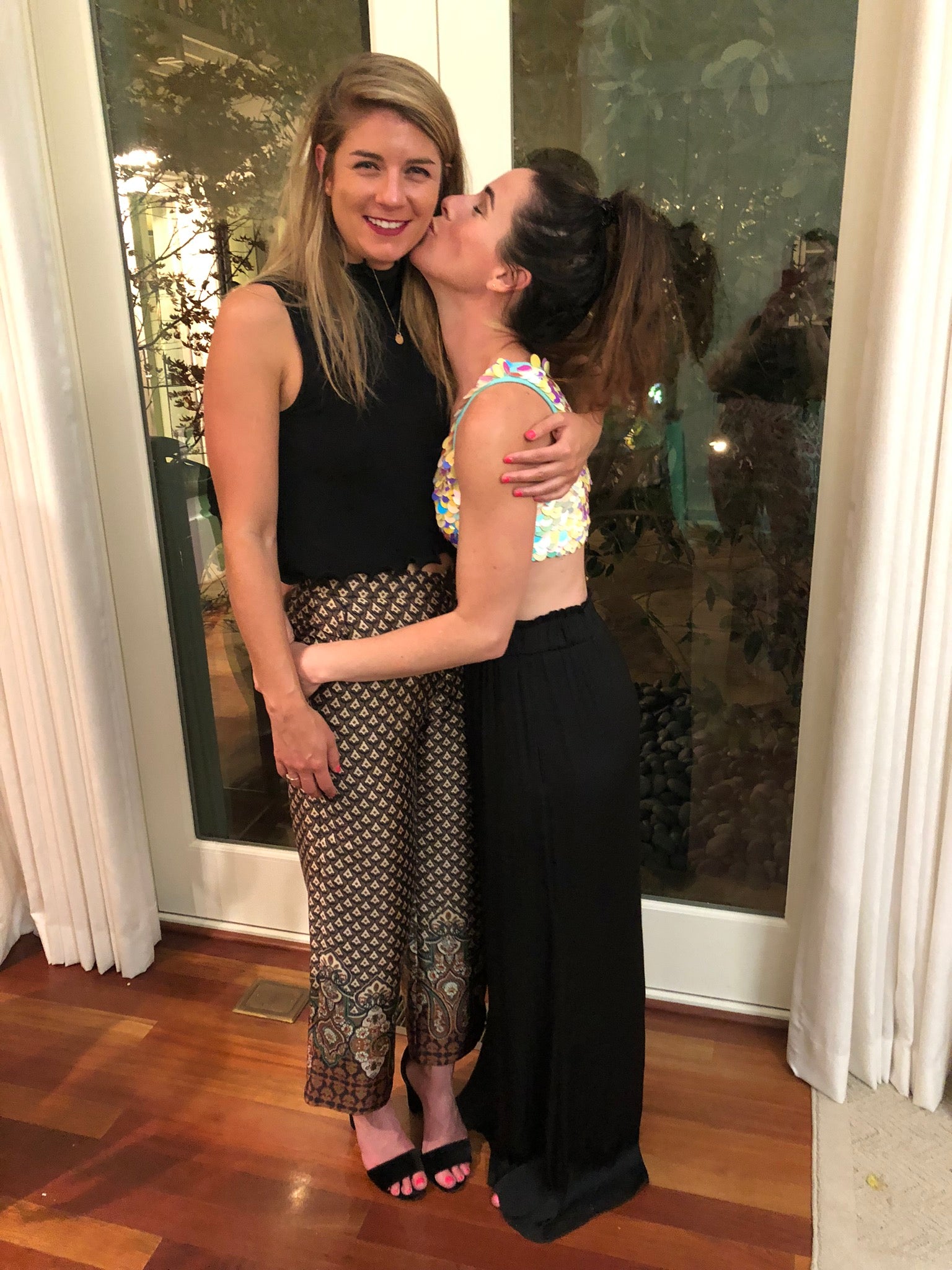 Woman in pearl sequin crop top kisses friend on the cheek