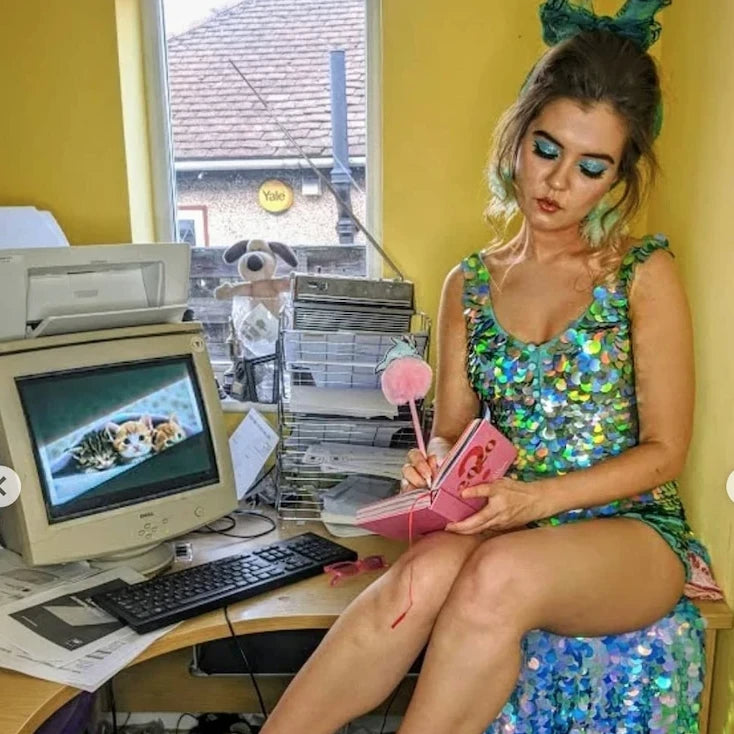 Woman in a green sequin playsuit sits in a home office