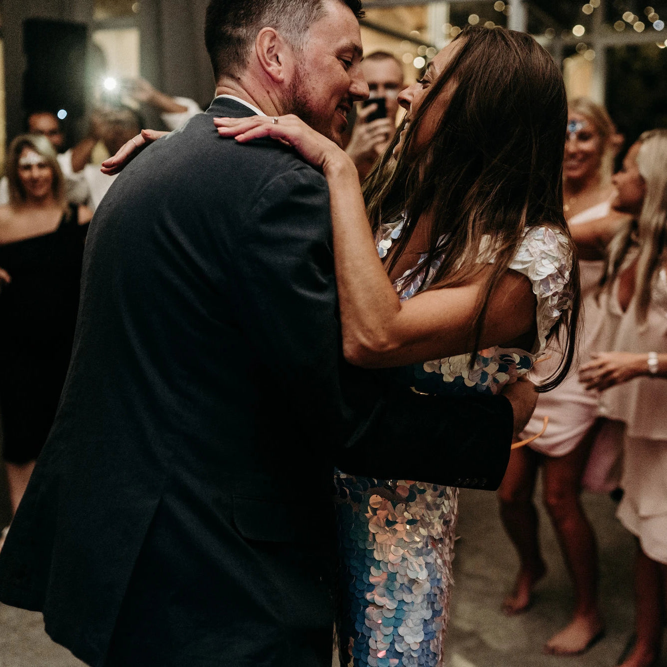 A bride in a white sequin jumpsuit dances with the groom