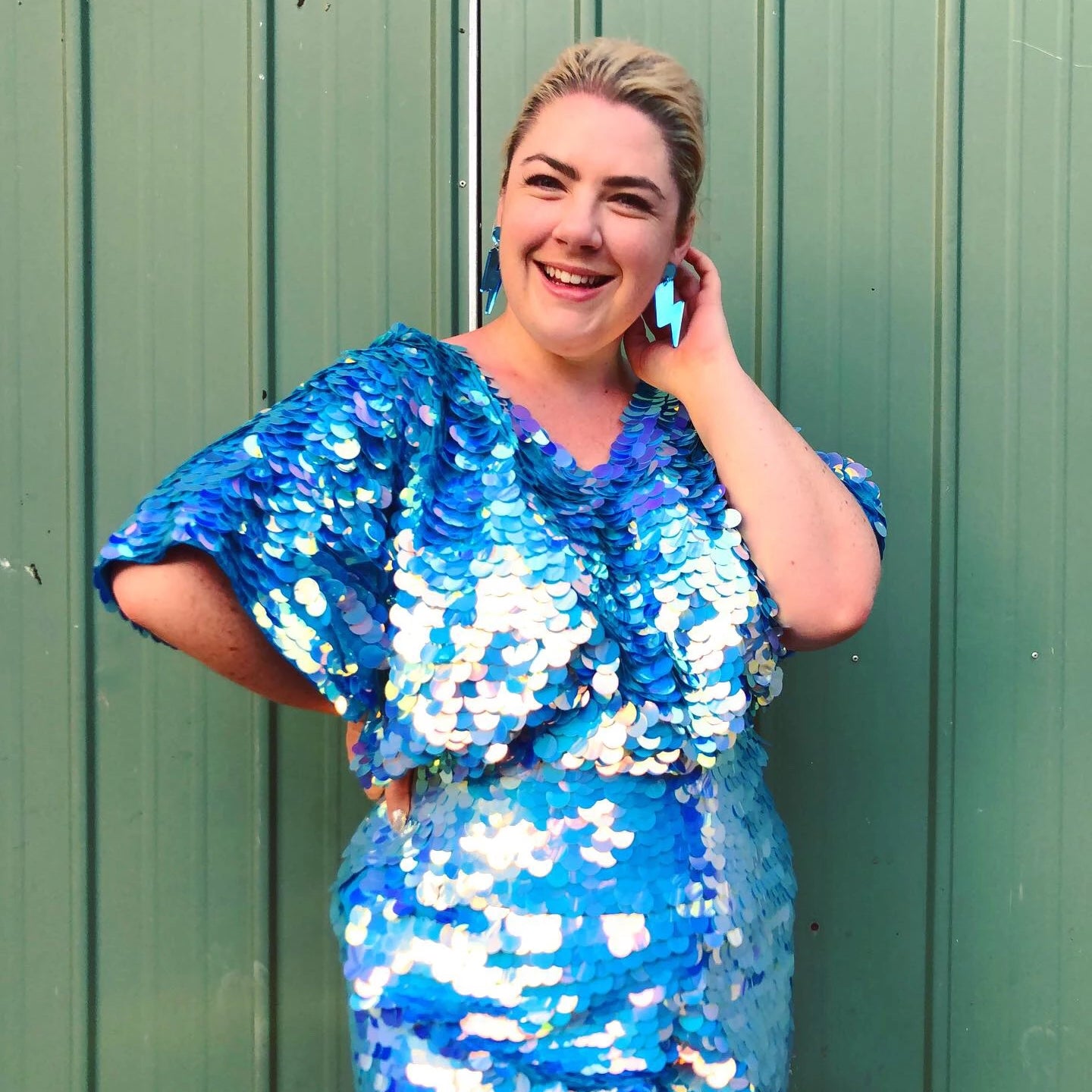 A woman in a blue sequin outfit poses against a green backdrop