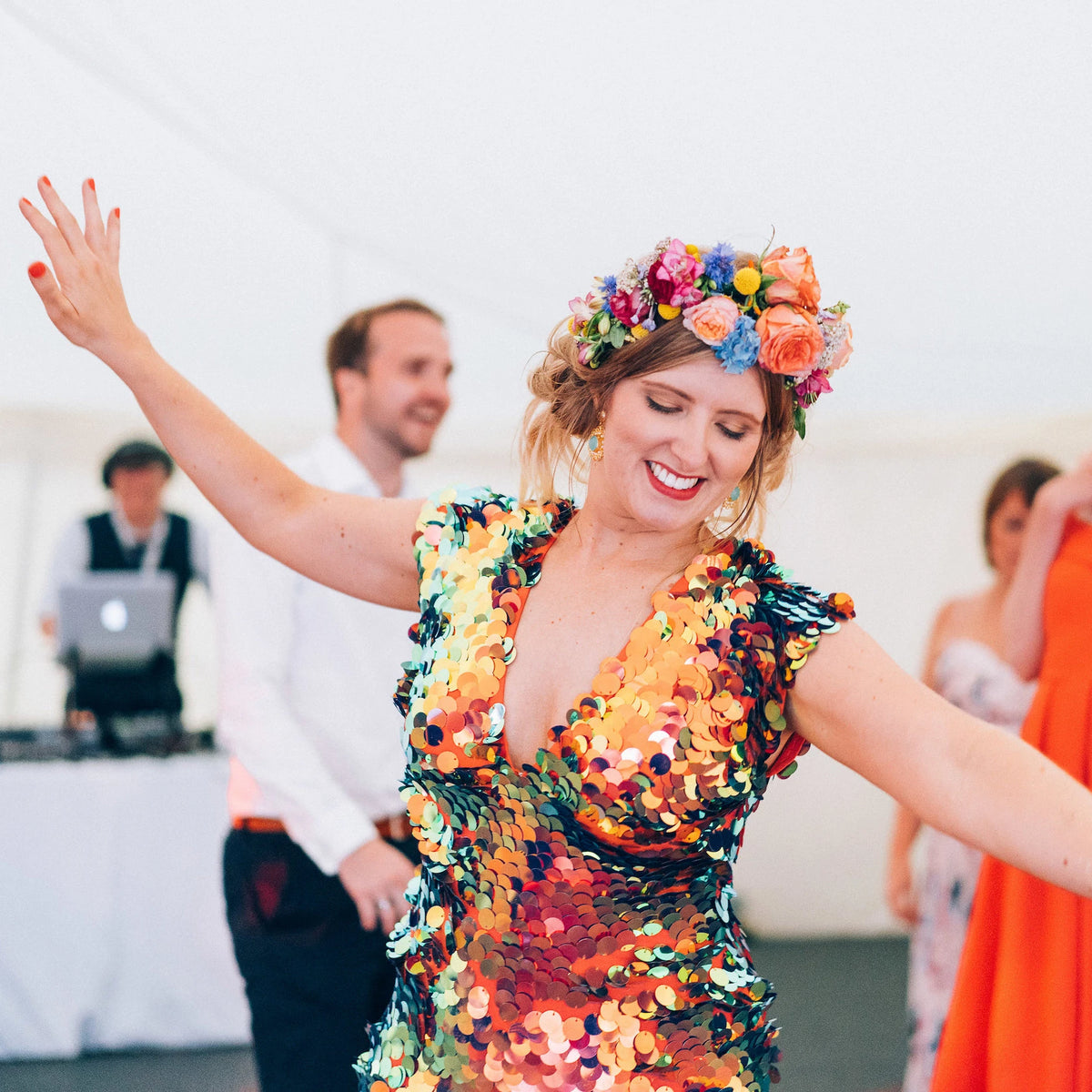 A bride with festival style flower crown and red sequin jumpsuit dances at her wedding