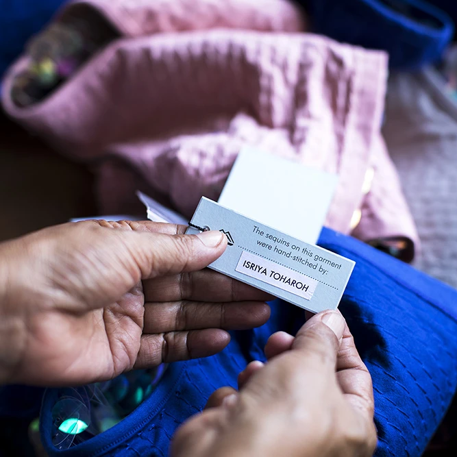 A woman working for slow fashion brand Rosa Bloom presents a clothing label that credits her as the person who made the garment. 