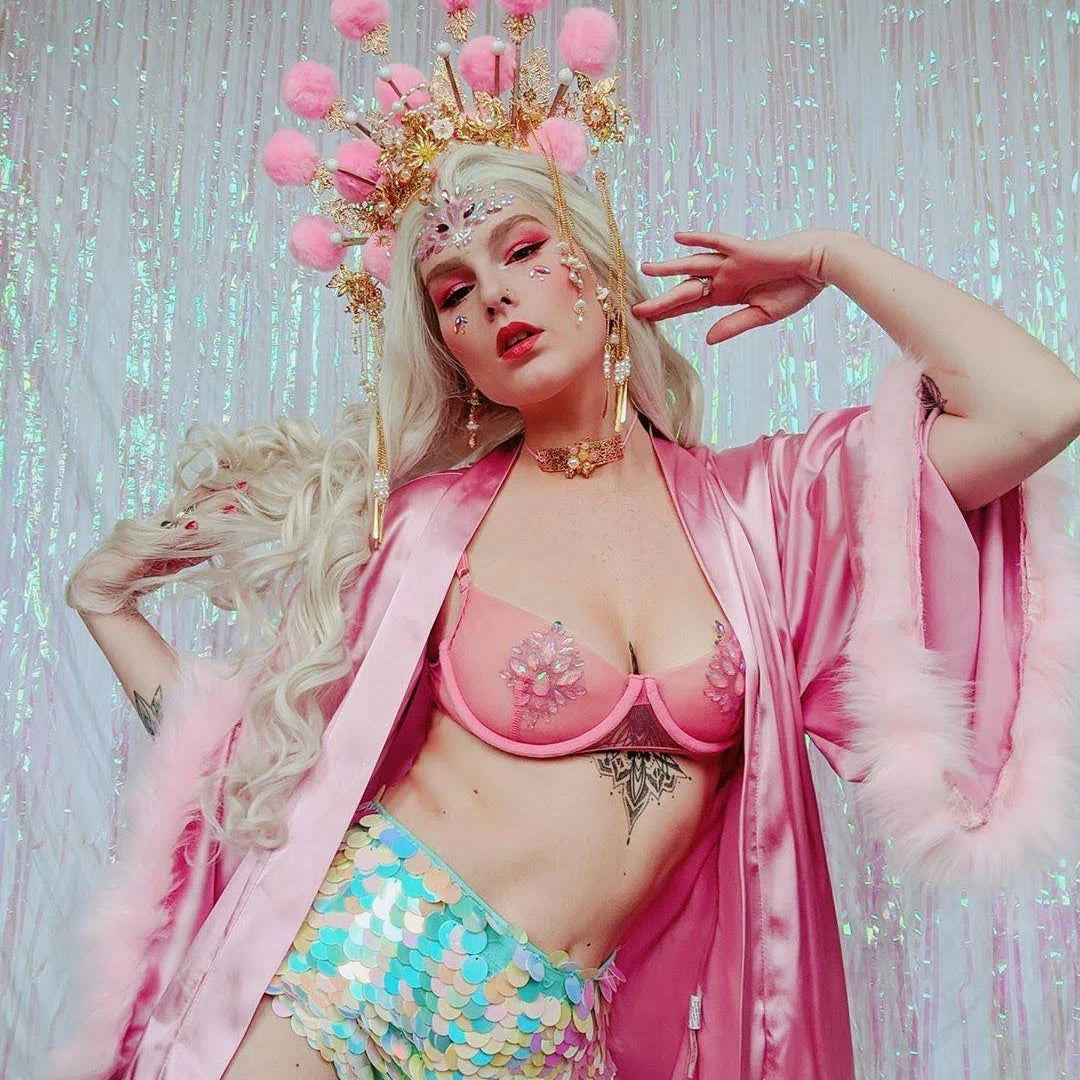 Woman wearing blue sequin hotpants and a pink fluffy headpiece with a pink kimono poses against a sparkly backdrop