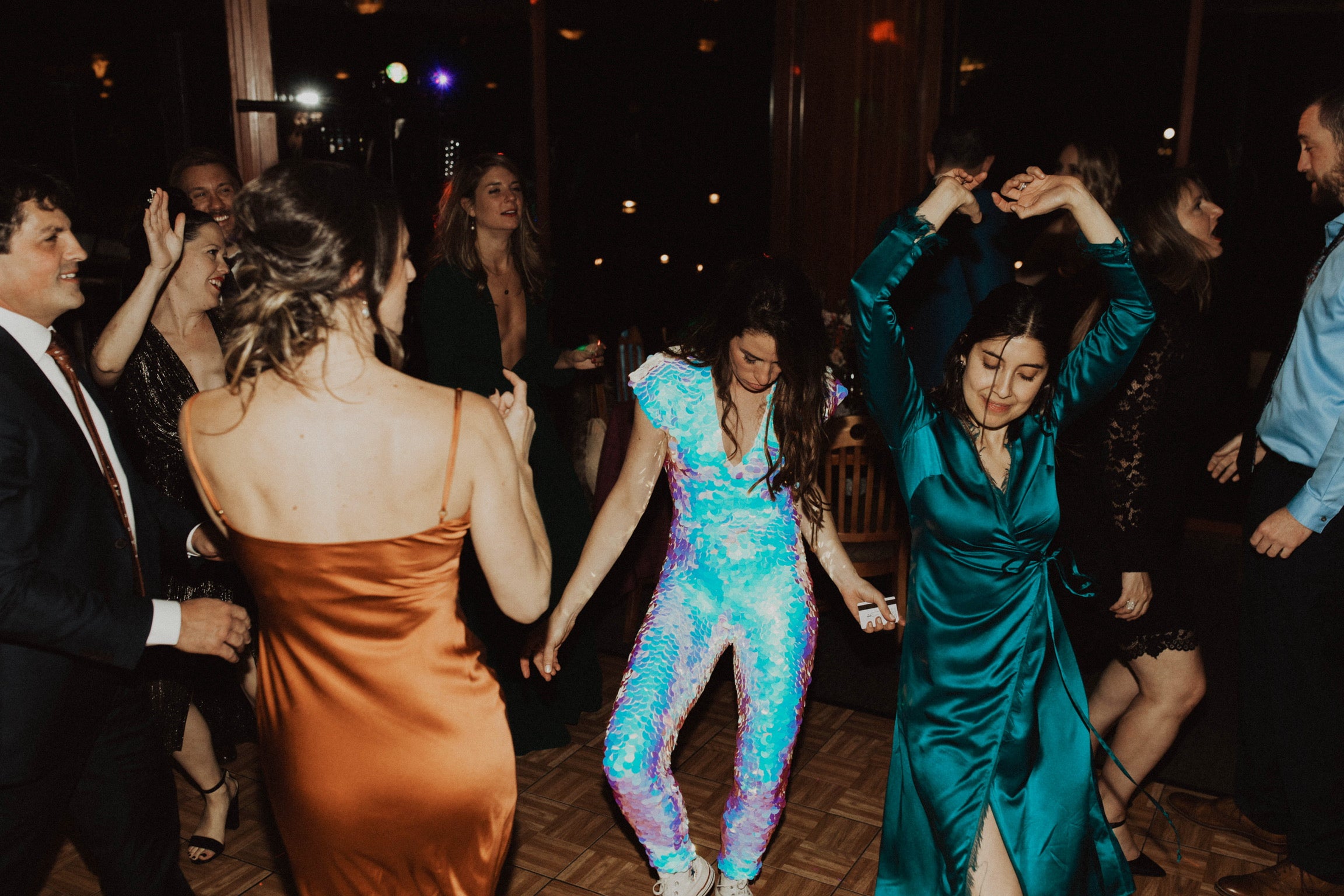 Woman in Opal sequin jumpsuit dances with friends at her wedding