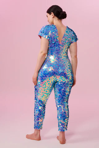 A woman wearing a multi colour blue sequin jumpsuit poses for the camera.
