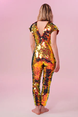 A woman wearing an orange and gold sequin catsuit poses with her back to the camera.