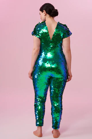 A woman wearing an emerald sequin jumpsuit poses with her back to the camera.