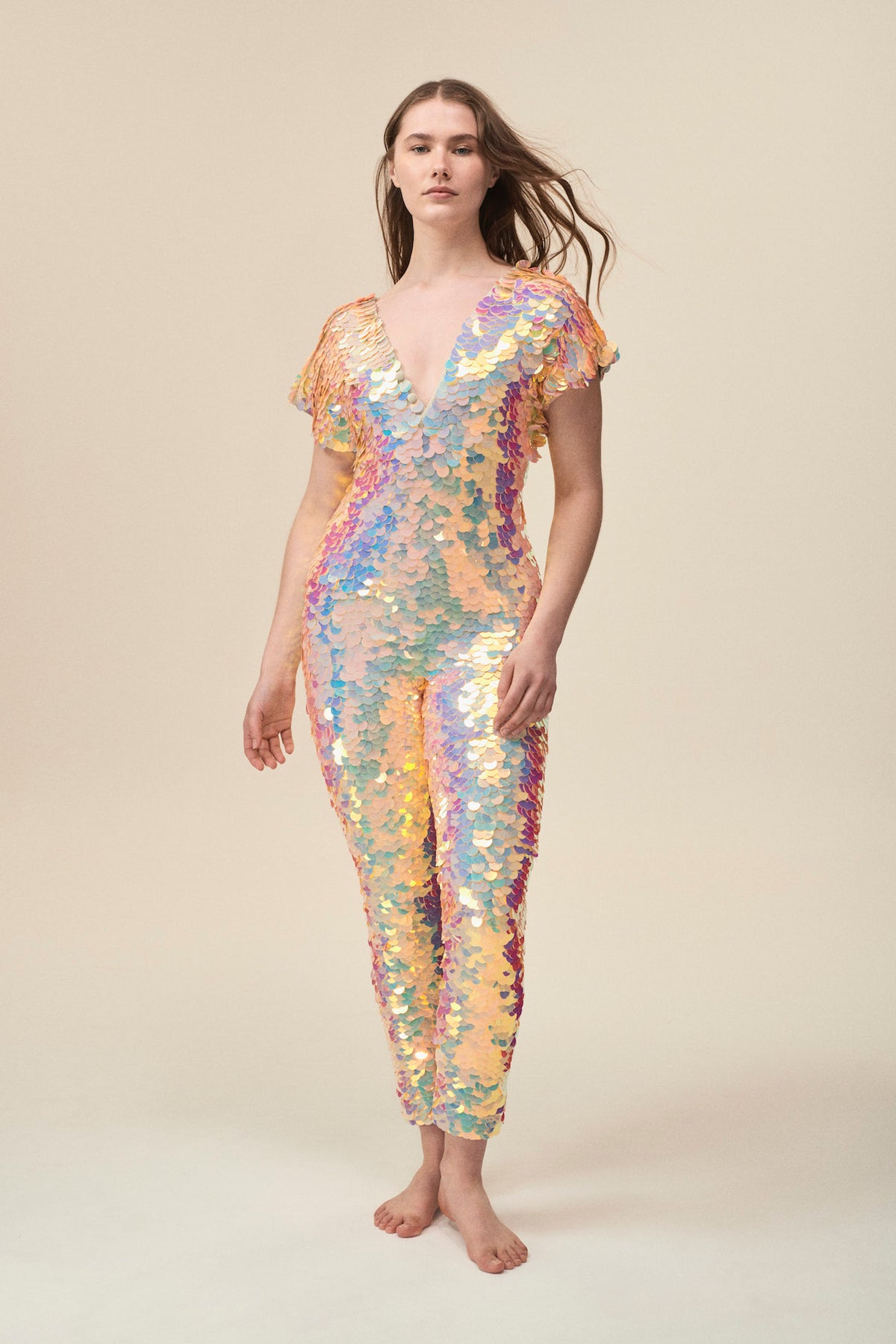 A woman wearing an off-white and pale pink sequin jumpsuit poses for the camera.