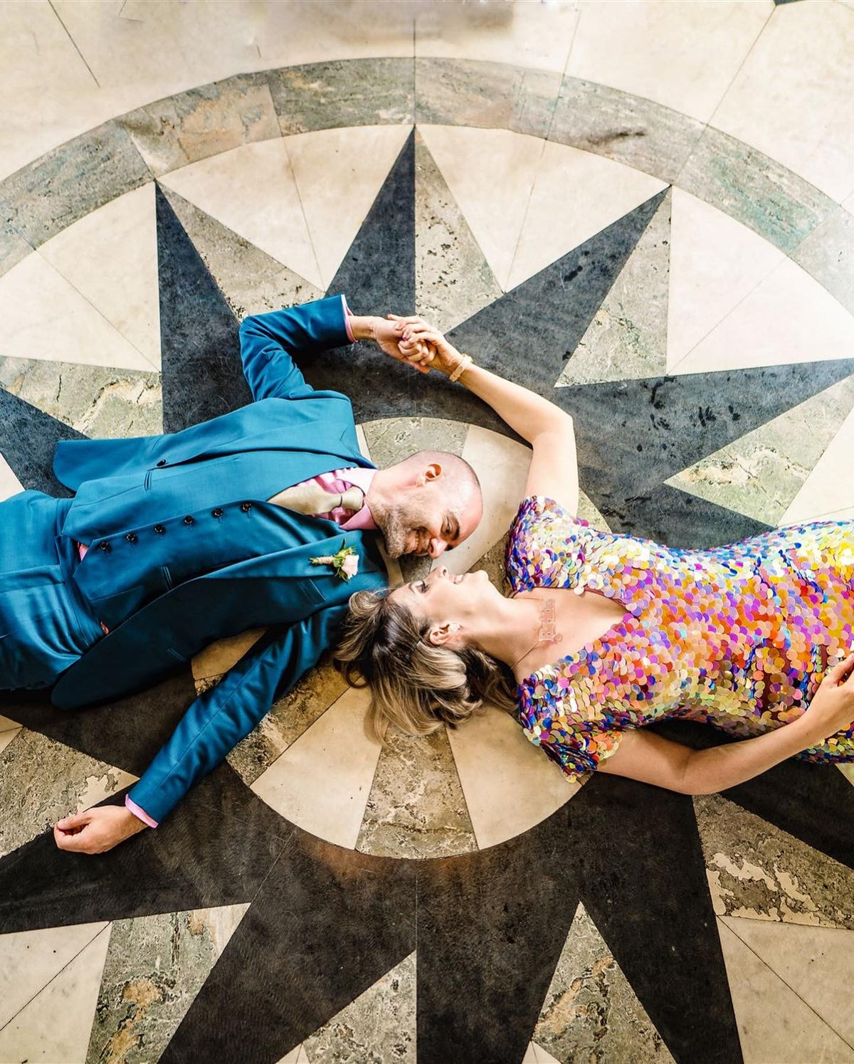 A bride wearing a sequin jumpsuit and her husband pictured laying on a star shaped flooring.