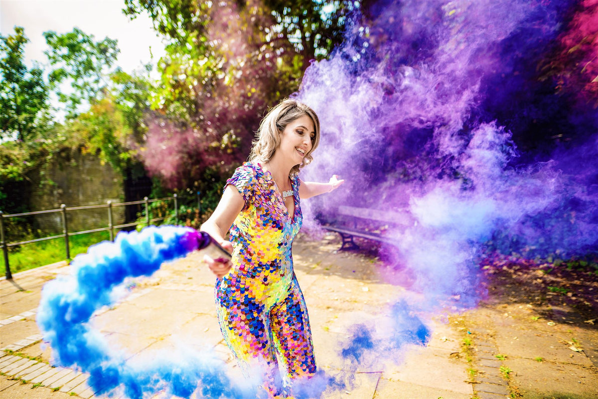 A woman dances in a purple and gold jumpsuit while she holds a smoke canon what 