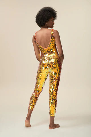 A woman wearing a bright coral sequin jumpsuit poses for the camera.