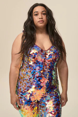 A plus sized woman wearing a purple and gold sequin catsuit poses for the camera.