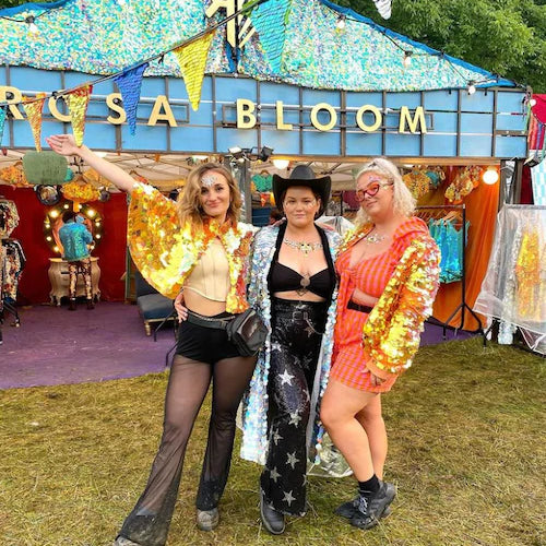 Three festival goers wearing bright coral sequin outfits pose outside the Rosa Bloom festival clothing shop.