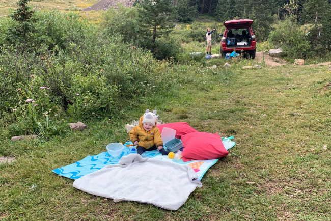 a toddler sitting on a blanket at a campsite