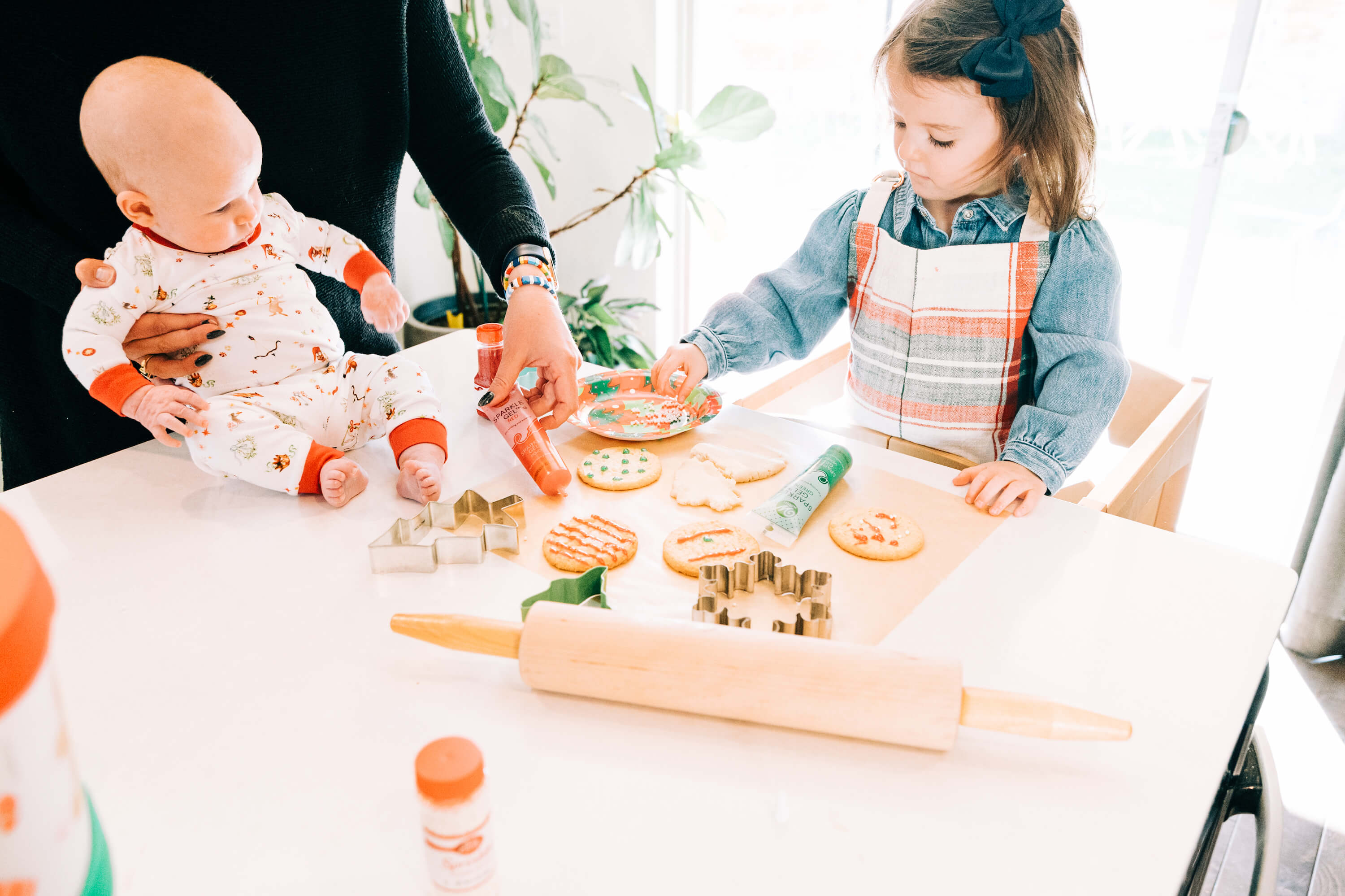 parent baking holiday themed cookies with her two little ones 