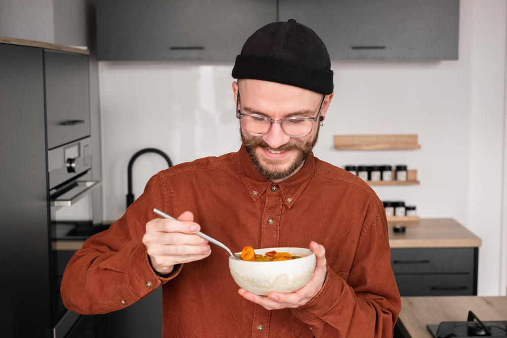 Mitarbeiter Jan lächelt und schaut dabei auf die Schale in seiner Hand in der die italienische Minestrone ist