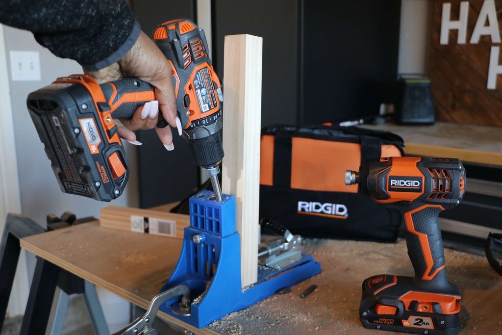 Using the Ridgid 18V Drill/Driver to drill pocket holes into 2x2 lumber on top of a plywood board beside the RIDGID Impact Driver and RIDGID Tool bag