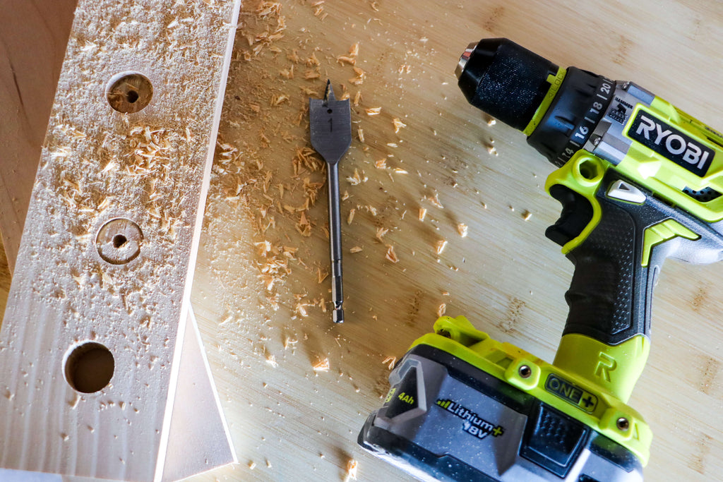 Ryobi Drill laying next to a spade bit and piece of wood