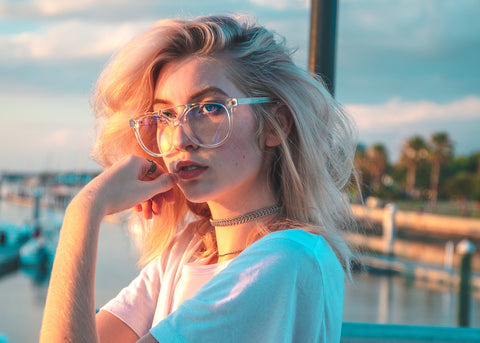 Blonde haired women wearing blue light lenses with a pensive look on her face looking off into the distance