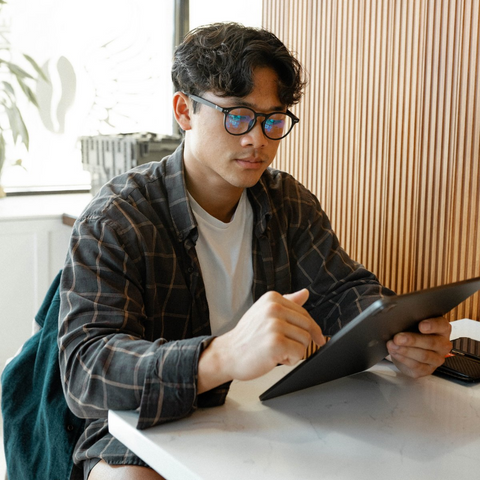 Man sitting in Coffee shop wearing glasses and looking at tablet